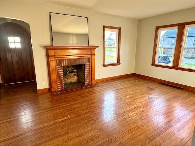 unfurnished living room with hardwood / wood-style floors, a healthy amount of sunlight, visible vents, and a brick fireplace