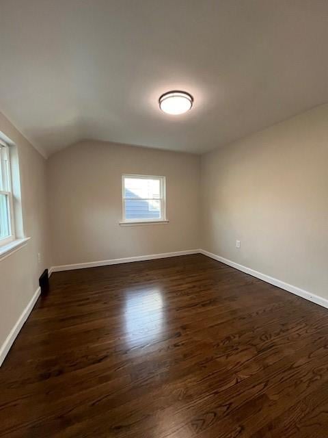 empty room featuring dark wood-style flooring, lofted ceiling, and baseboards