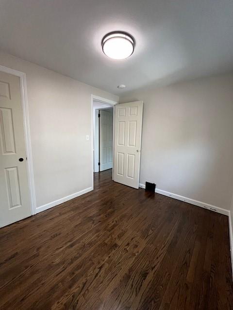 spare room featuring baseboards and dark wood finished floors
