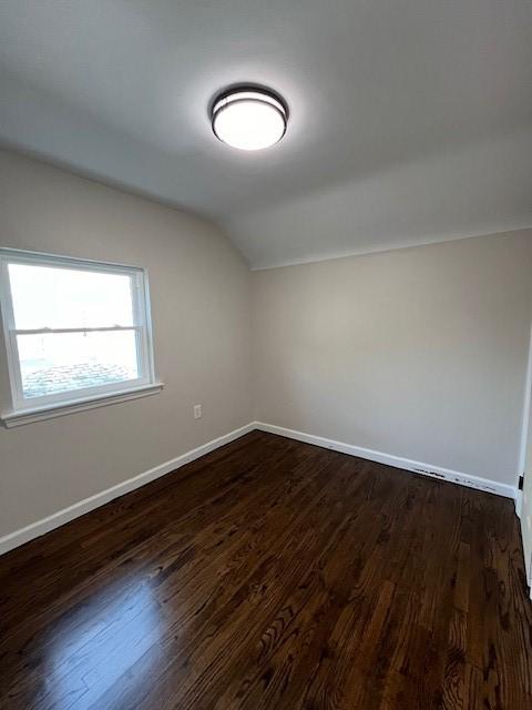 additional living space with dark wood finished floors, vaulted ceiling, and baseboards