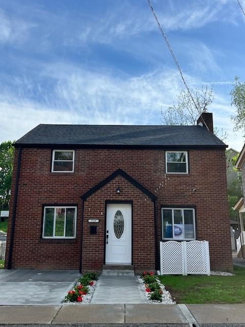 view of property with a shingled roof, a chimney, and brick siding