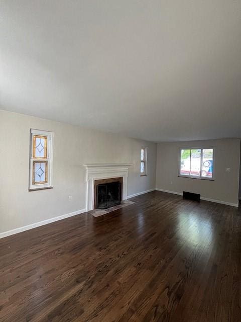 unfurnished living room featuring dark wood-style flooring, baseboards, and a fireplace with flush hearth