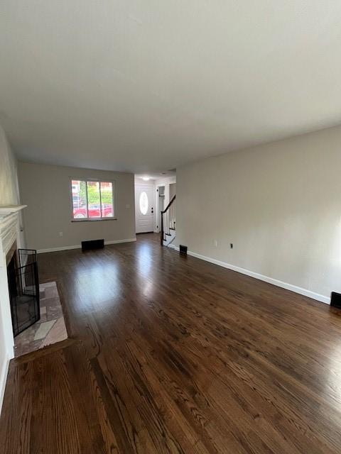 unfurnished living room with a fireplace, dark wood-style flooring, stairs, and baseboards