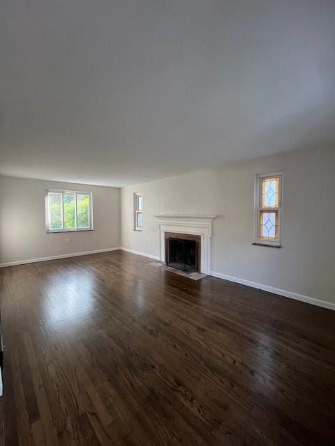 unfurnished living room featuring baseboards, a fireplace with flush hearth, and dark wood finished floors