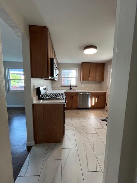 kitchen featuring brown cabinets, baseboards, light countertops, appliances with stainless steel finishes, and marble finish floor
