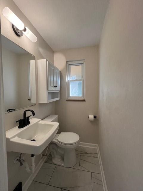 half bathroom featuring toilet, marble finish floor, baseboards, and a sink