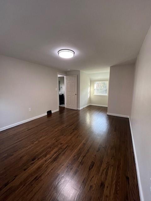 unfurnished room with baseboards and dark wood-style floors