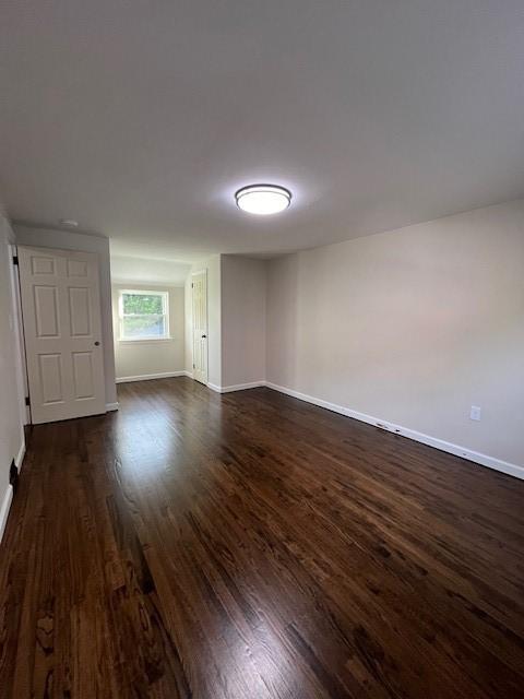 spare room with baseboards and dark wood-style floors
