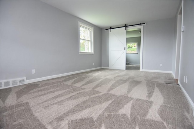 unfurnished bedroom featuring multiple windows, visible vents, a barn door, and carpet floors