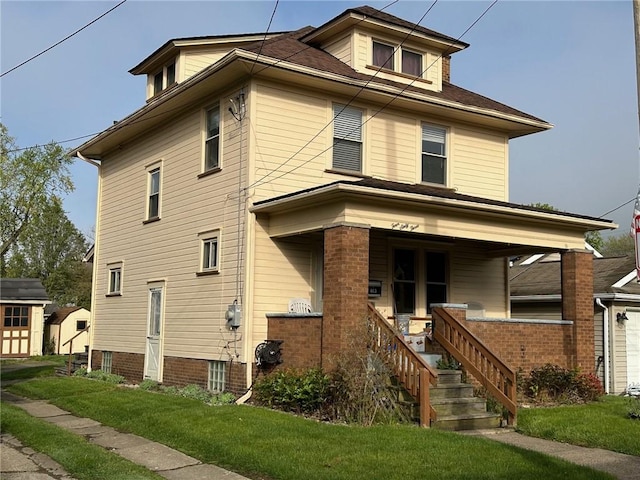 american foursquare style home with a front yard, a porch, an outbuilding, and a storage shed