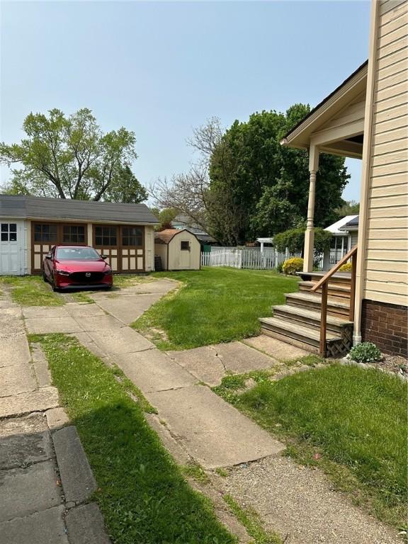 view of yard with concrete driveway, an outdoor structure, fence, and a shed