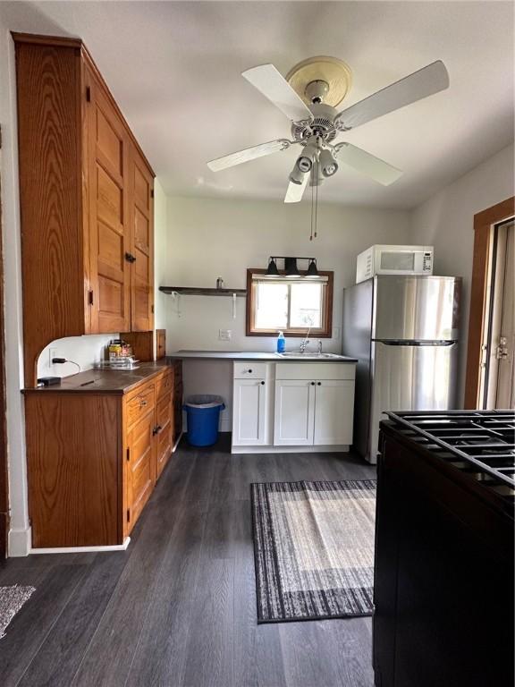 kitchen featuring freestanding refrigerator, dark wood-style flooring, ceiling fan, white microwave, and black range oven