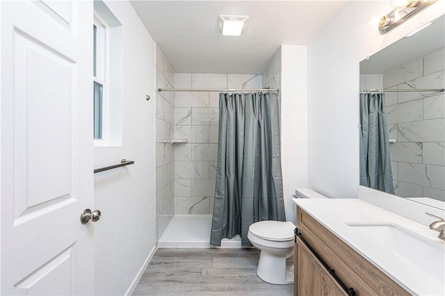 bathroom with toilet, baseboards, tiled shower, vanity, and wood finished floors