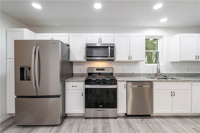 kitchen featuring light wood-style flooring, a sink, stainless steel appliances, white cabinets, and light stone counters