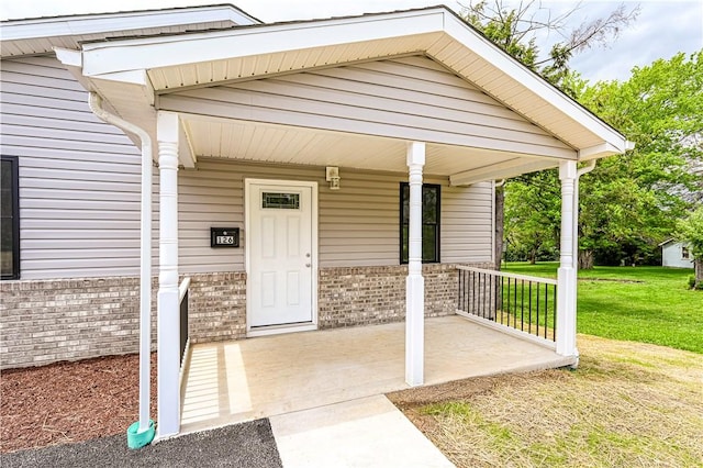 view of exterior entry featuring a lawn, a porch, and brick siding