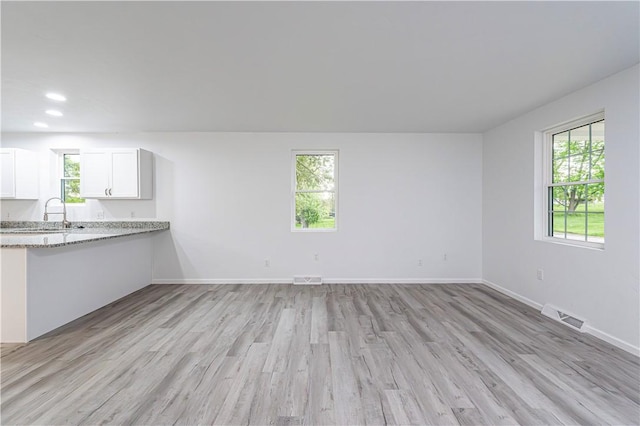 unfurnished living room with baseboards, light wood finished floors, visible vents, and a sink