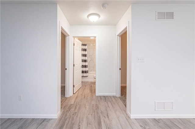 corridor with baseboards, visible vents, and light wood-style floors