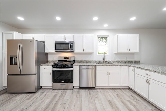 kitchen with light wood finished floors, a sink, white cabinets, light stone countertops, and appliances with stainless steel finishes