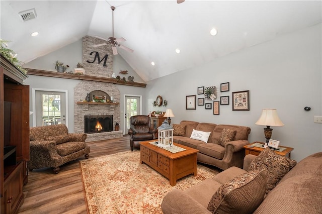 living room with a ceiling fan, visible vents, high vaulted ceiling, light wood-type flooring, and a large fireplace