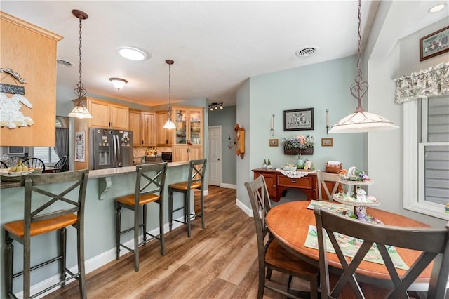 kitchen featuring a kitchen breakfast bar, light wood finished floors, stainless steel fridge, light brown cabinets, and baseboards