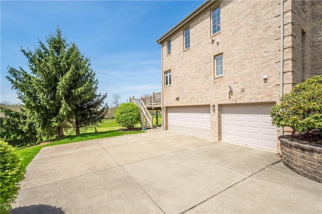 view of side of home with an attached garage, brick siding, driveway, and stairs