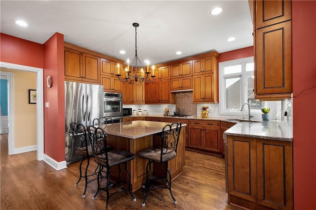 kitchen featuring wood finished floors, a sink, brown cabinetry, a kitchen breakfast bar, and appliances with stainless steel finishes