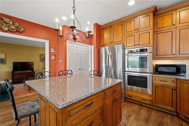 kitchen featuring a notable chandelier, light stone countertops, brown cabinets, stainless steel appliances, and dark wood-style floors