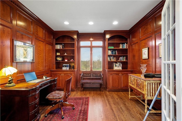 home office featuring light wood finished floors, crown molding, built in study area, and built in shelves