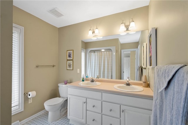 bathroom with double vanity, toilet, a sink, visible vents, and baseboards