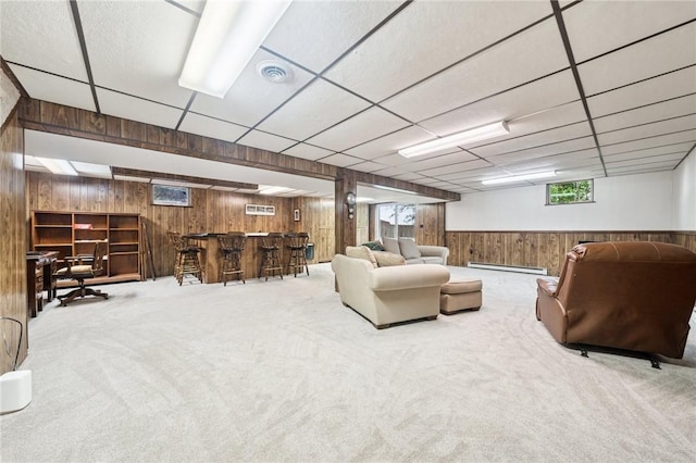 carpeted living area with wooden walls, bar area, and a baseboard heating unit