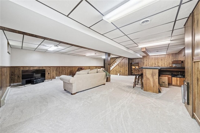 living room with stairway, light colored carpet, wooden walls, and visible vents