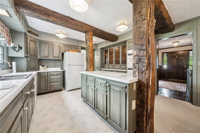kitchen featuring freestanding refrigerator, a textured ceiling, cooktop, a sink, and light countertops