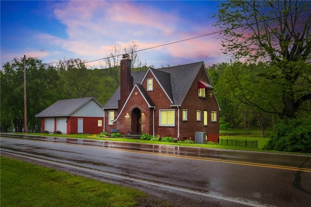 english style home with a chimney, driveway, brick siding, a garage, and central air condition unit
