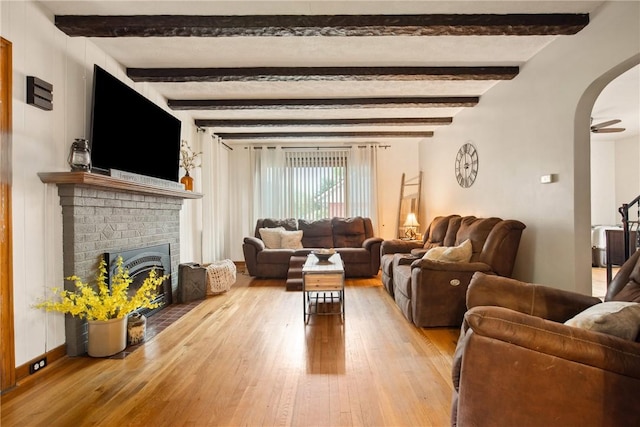living room featuring a fireplace, ceiling fan, wood-type flooring, arched walkways, and beamed ceiling