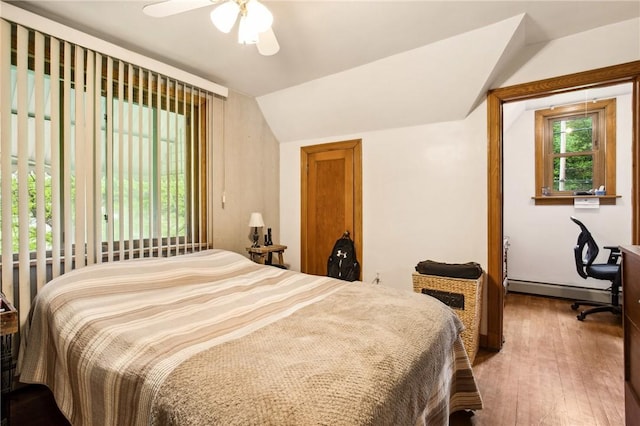 bedroom with a baseboard heating unit, lofted ceiling, hardwood / wood-style floors, and a ceiling fan