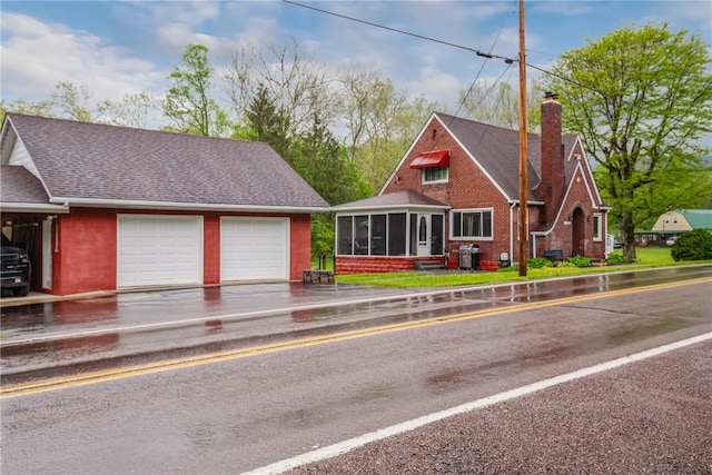 view of front of property featuring a chimney, a shingled roof, a sunroom, and a garage