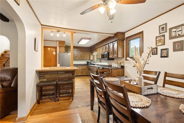 dining area featuring a ceiling fan, stairway, light wood-style flooring, and arched walkways