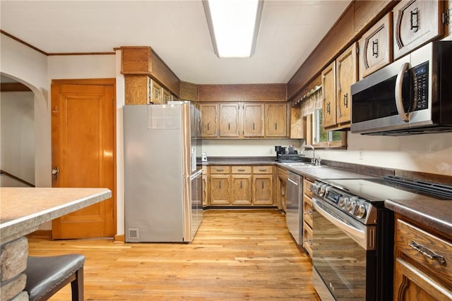 kitchen with light wood finished floors, a sink, arched walkways, dark countertops, and stainless steel appliances