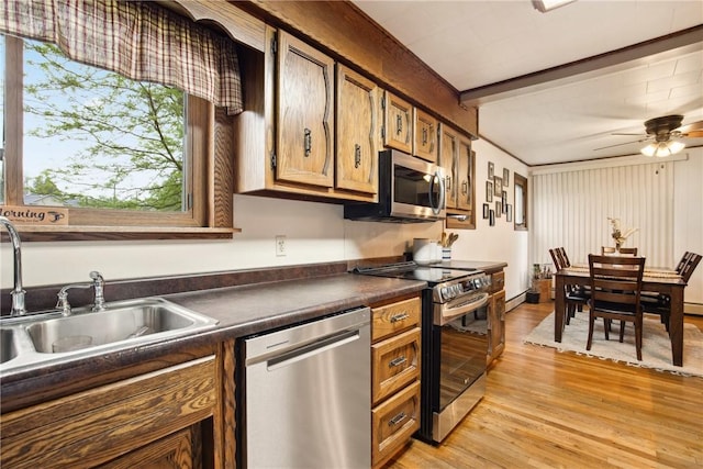 kitchen with a sink, dark countertops, stainless steel appliances, light wood-type flooring, and ceiling fan