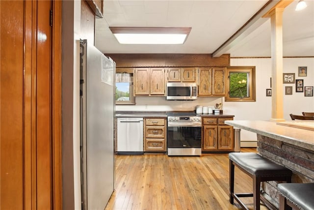 kitchen featuring light wood-style flooring, brown cabinets, dark countertops, and appliances with stainless steel finishes