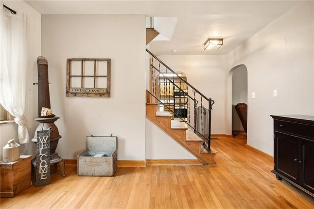 interior space with arched walkways, baseboards, light wood-type flooring, and stairway