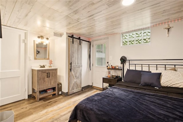bedroom featuring a barn door, wooden ceiling, baseboards, connected bathroom, and light wood-style floors