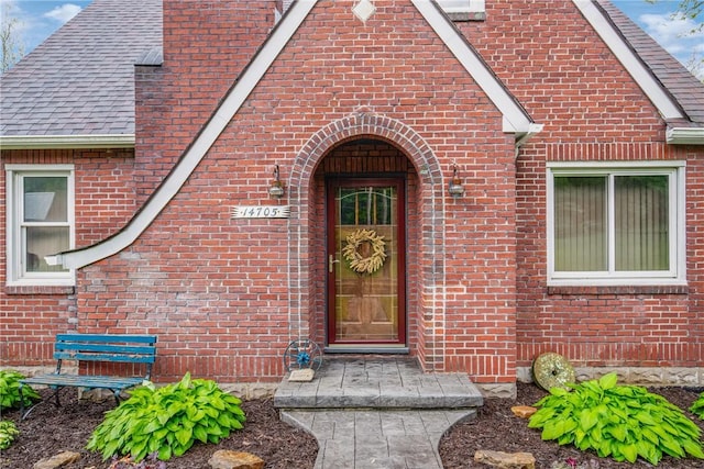 entrance to property featuring brick siding and roof with shingles