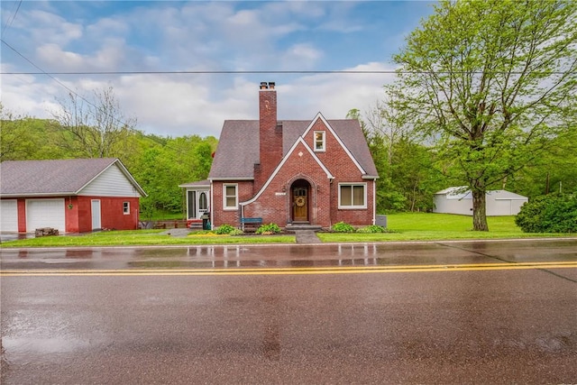 english style home with a chimney, an outbuilding, brick siding, and a front lawn