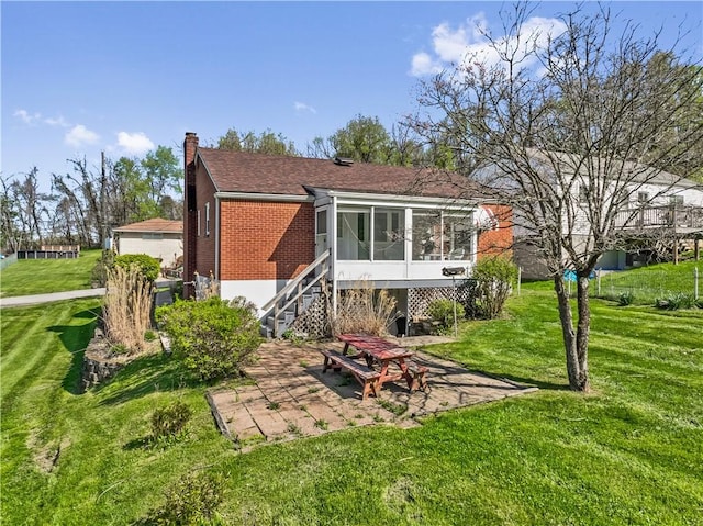 back of house with a sunroom, a yard, a chimney, a patio area, and roof with shingles