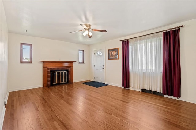 unfurnished living room with a fireplace, ceiling fan, baseboards, and wood finished floors