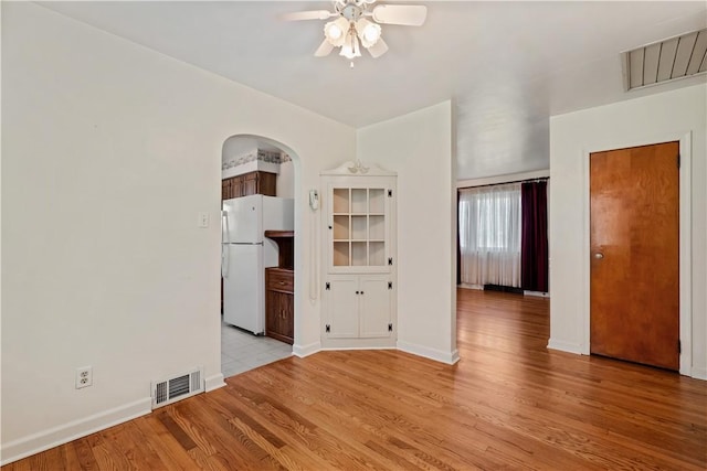 unfurnished room with visible vents, light wood-style flooring, a ceiling fan, and arched walkways