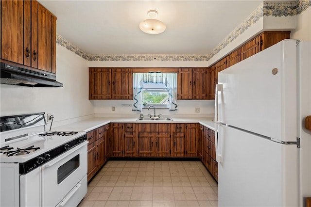 kitchen featuring under cabinet range hood, brown cabinets, a sink, and white appliances