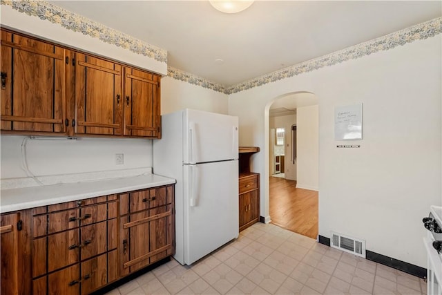 kitchen with brown cabinets, freestanding refrigerator, visible vents, arched walkways, and light countertops