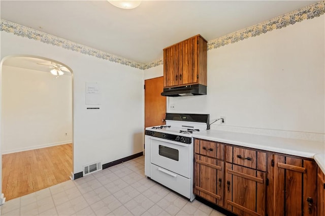 kitchen with under cabinet range hood, brown cabinetry, visible vents, arched walkways, and gas range gas stove